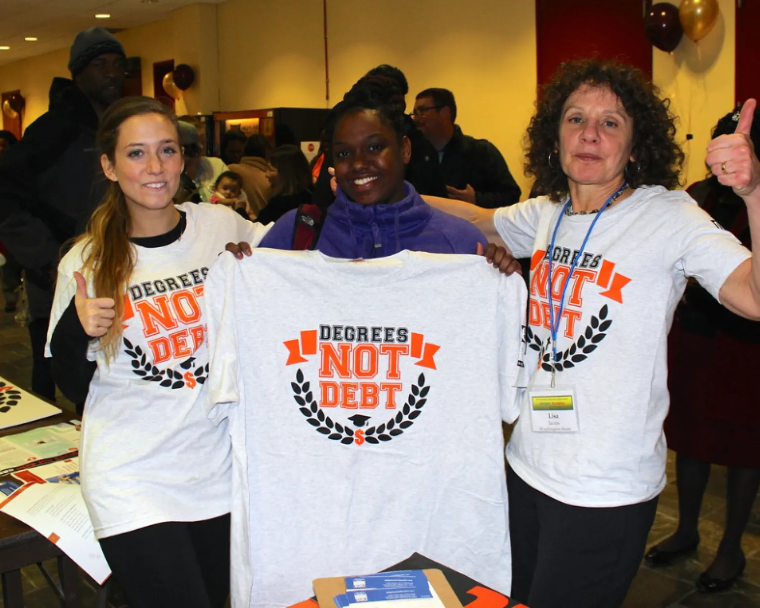 Two student teachers and a union staff-person stand with t-shirts that read "Degrees Not Debt."