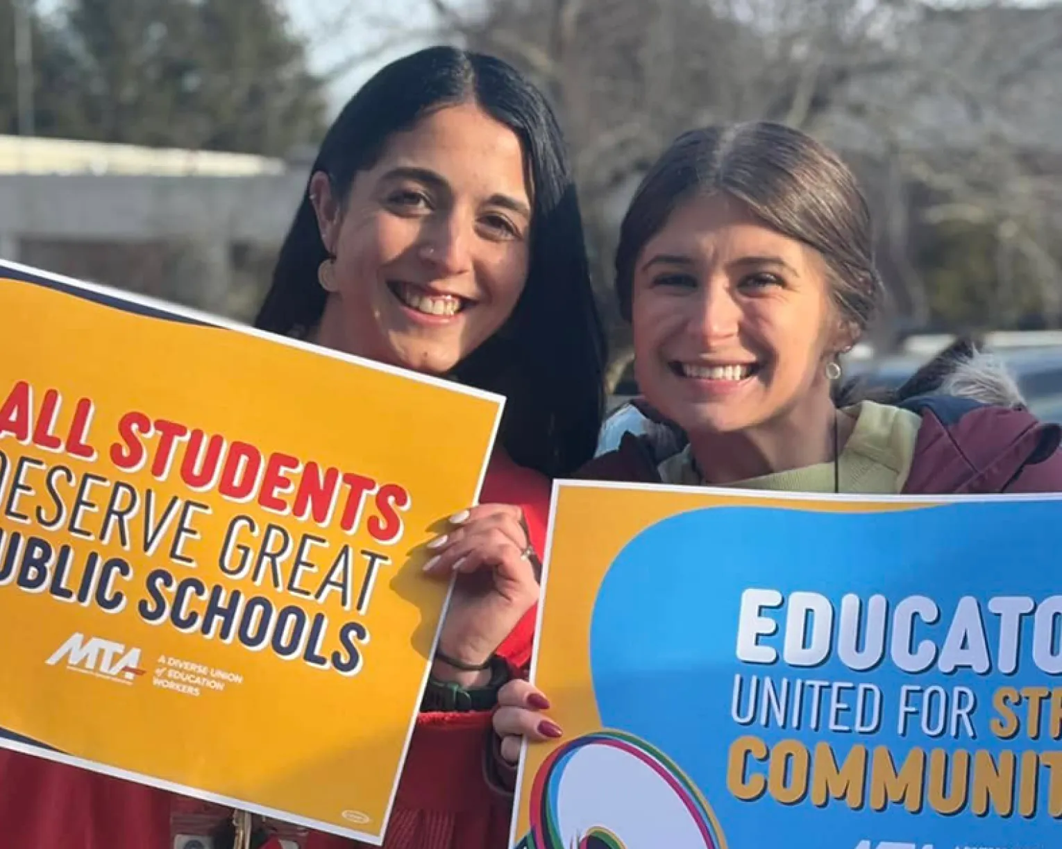 Two educators at an action in March 2025. They are holding signs that say "All Students Deserve a Great Public School" and "Educators United for Strong Communities."