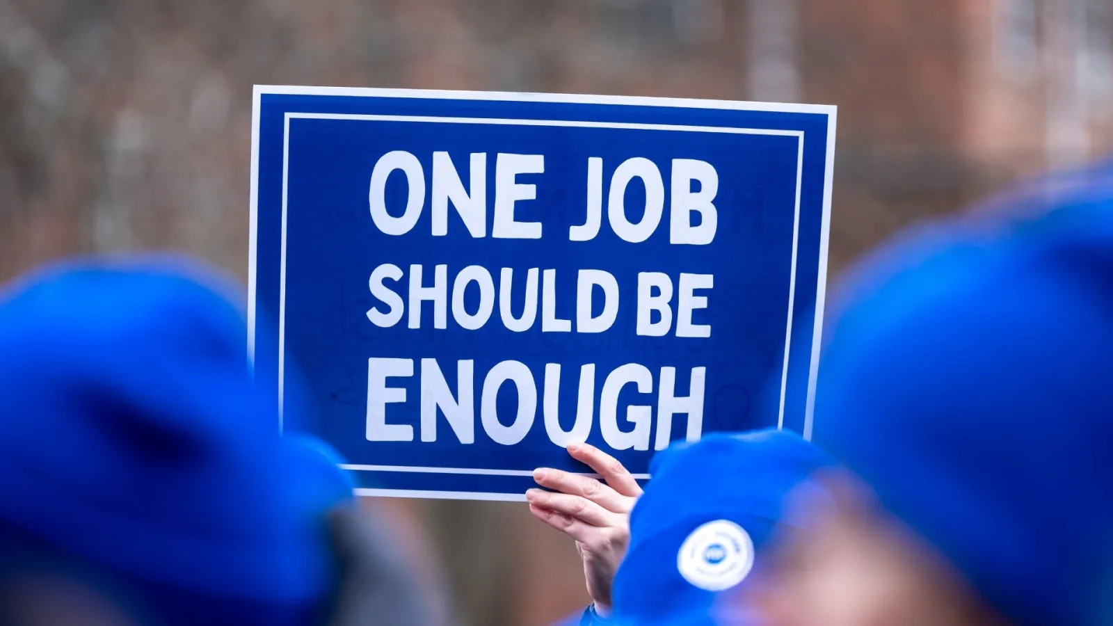A protest sign at a rally that reads “One job should be enough.” Newton, MA.